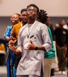 A guest in a pale kaftan applauding in the crowd.